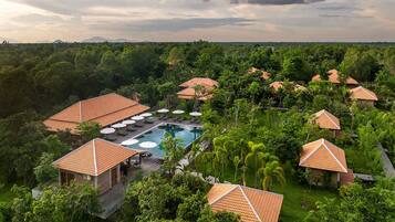 A resort with multiple bungalow-style buildings, a central swimming pool, and lush greenery surrounding the property.