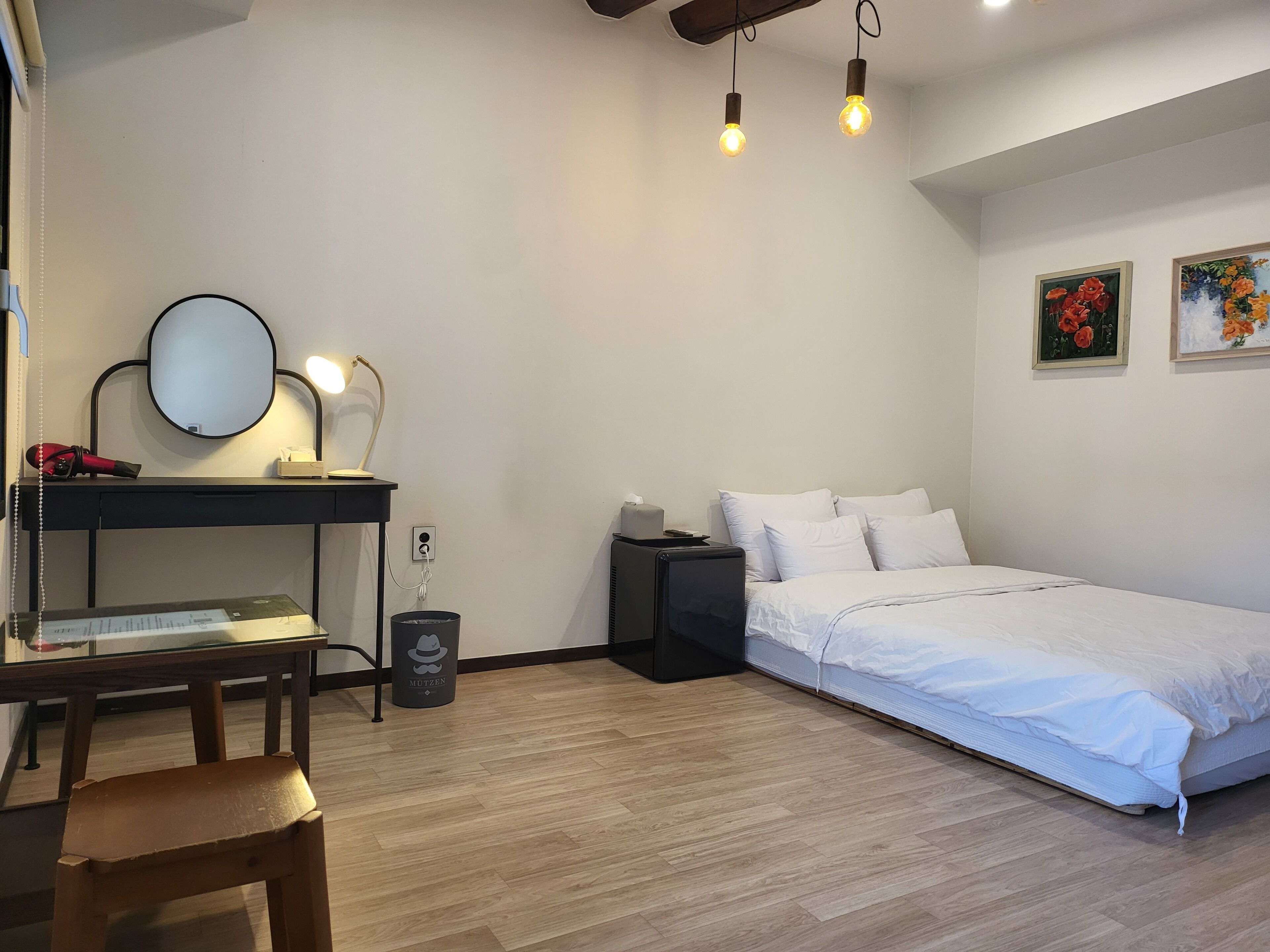 A bedroom with a bed, a desk with a mirror, a chair, and a trash bin.