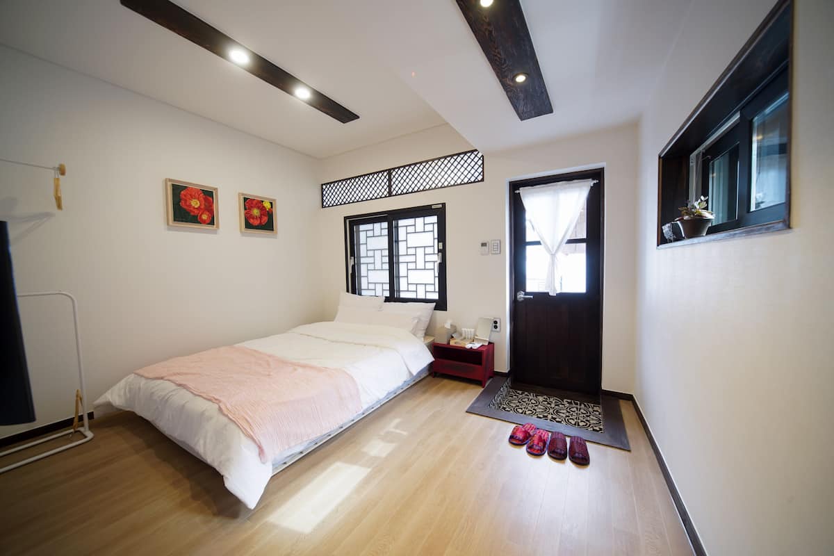 A bedroom with a bed, a nightstand, a window with a view, and a door.