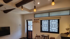A room with a wooden floor, a TV mounted on the wall, a window with a lattice design, and a small table with a lamp. - Naganjae (Gyeongju)