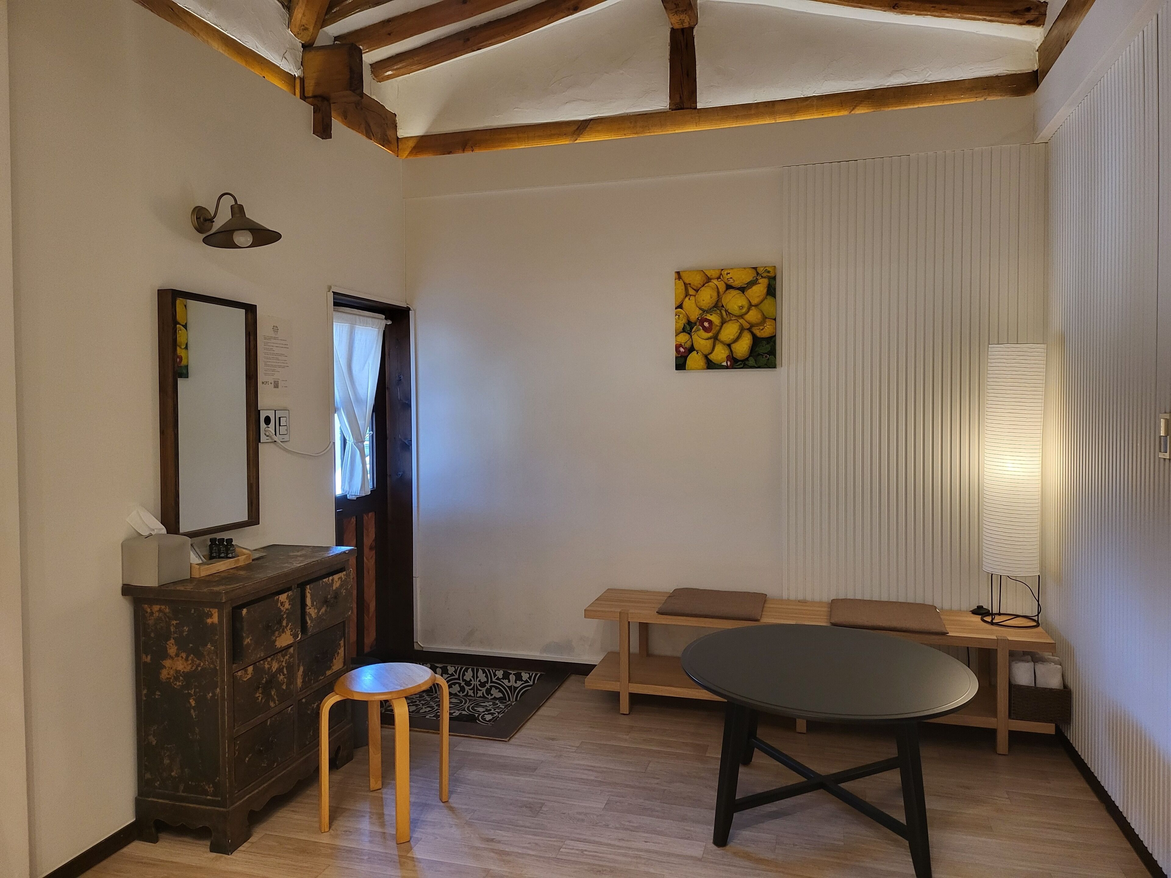A room with a wooden bench, a table, a mirror, a lamp, and a painting.