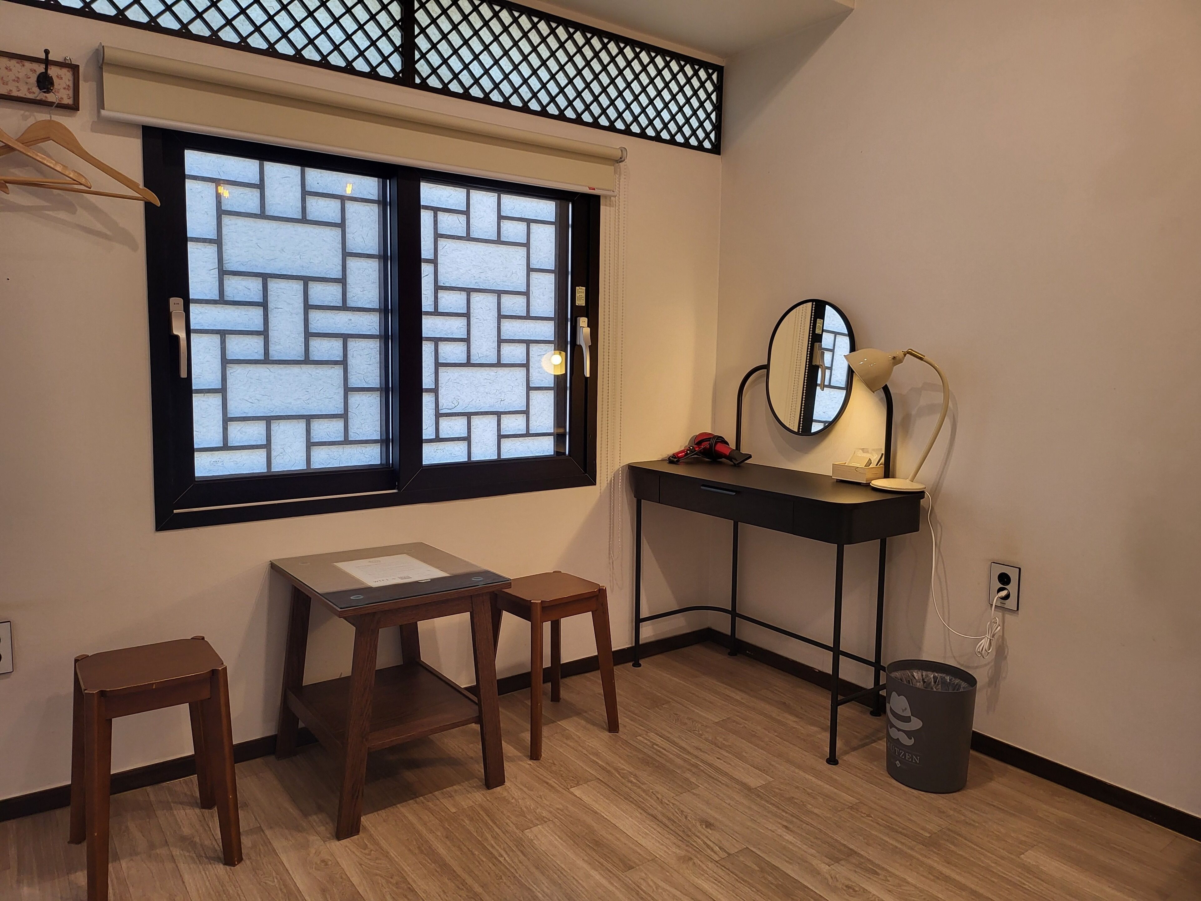 A room with a desk, two stools, a mirror, a lamp, and a window with a lattice design.