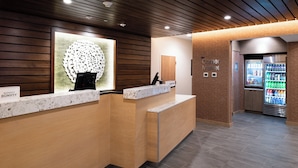 A hotel reception area with a marble counter, a decorative wall piece, and a vending machine. - Fairfield Inn & Suites by Marriott Charlotte University Research Park (Charlotte)