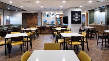 A restaurant with multiple tables and chairs, a bar area, and a kitchen visible in the background.