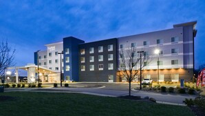 A multi-story hotel with a modern design, featuring a prominent entrance with a covered walkway and a well-lit facade. - Fairfield Inn & Suites by Marriott Charlotte University Research Park (Charlotte)