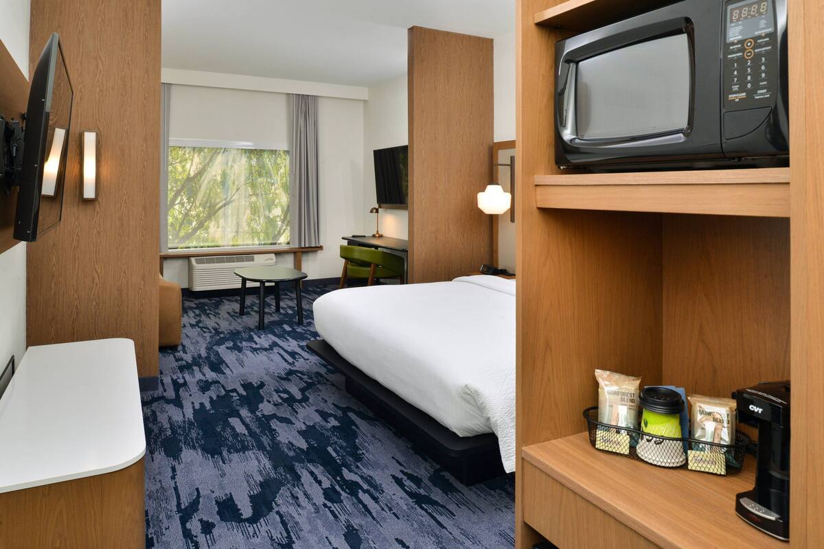 A hotel room with a bed, a desk, a chair, a TV, a microwave, and a coffee maker.
