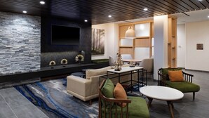 A modern living room with a stone accent wall, a flat-screen TV, a dining area, and comfortable seating. - Fairfield Inn & Suites by Marriott Charlotte University Research Park (Charlotte)
