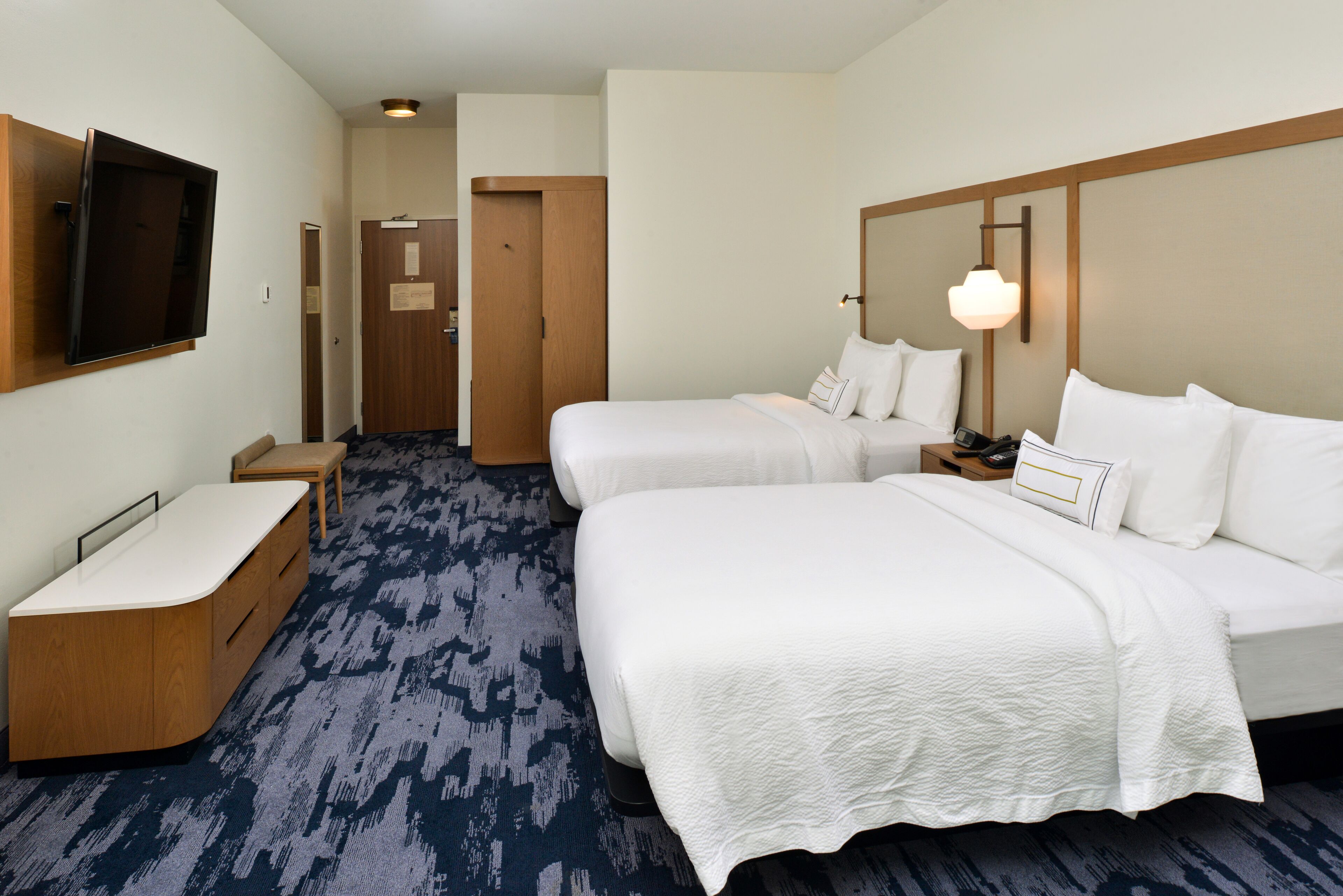 Une chambre d’hôtel avec deux lits, un téléviseur fixé au mur, un bureau et une porte donnant sur une autre chambre.
