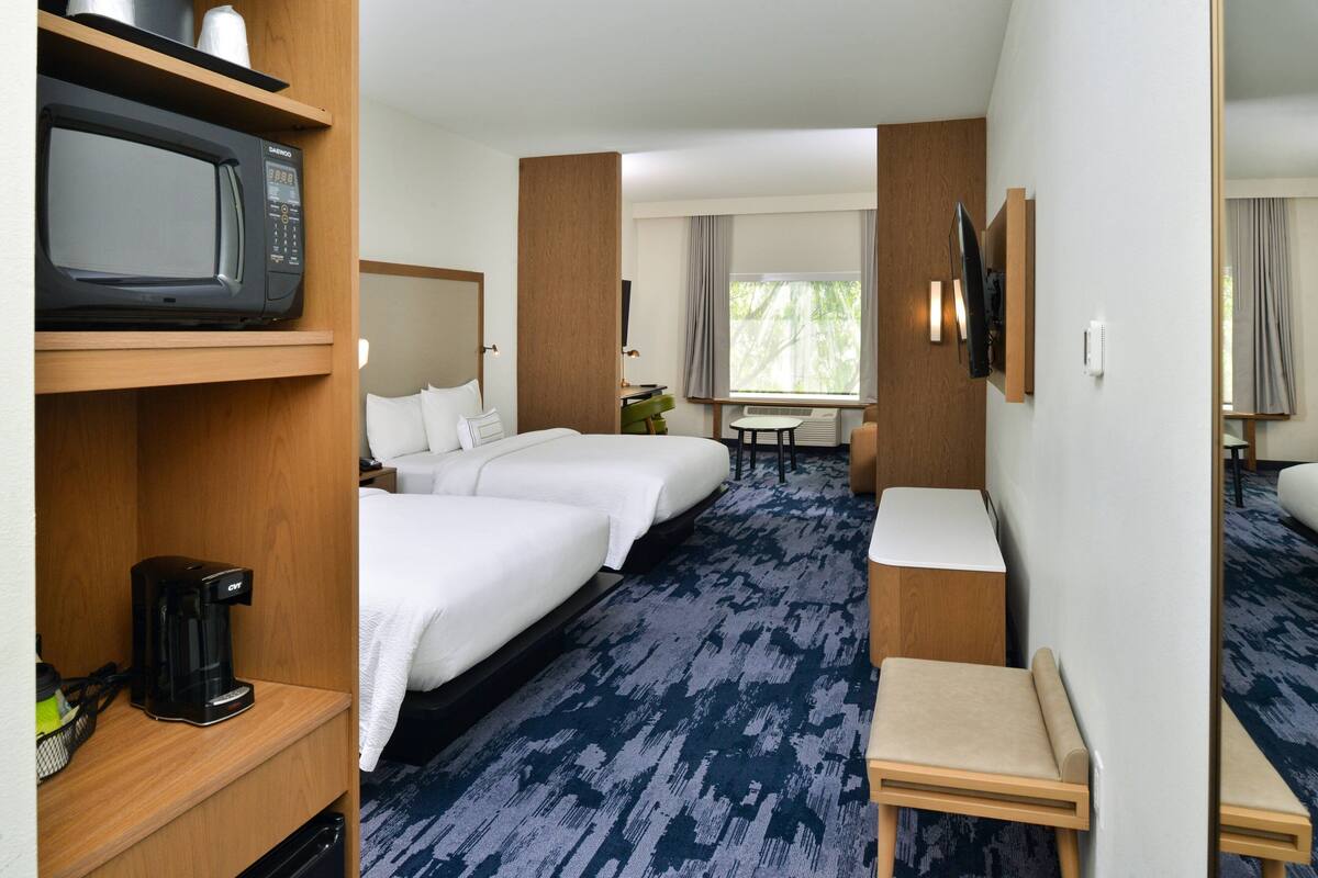 A hotel room with two beds, a microwave, a coffee maker, a TV, and a small table.