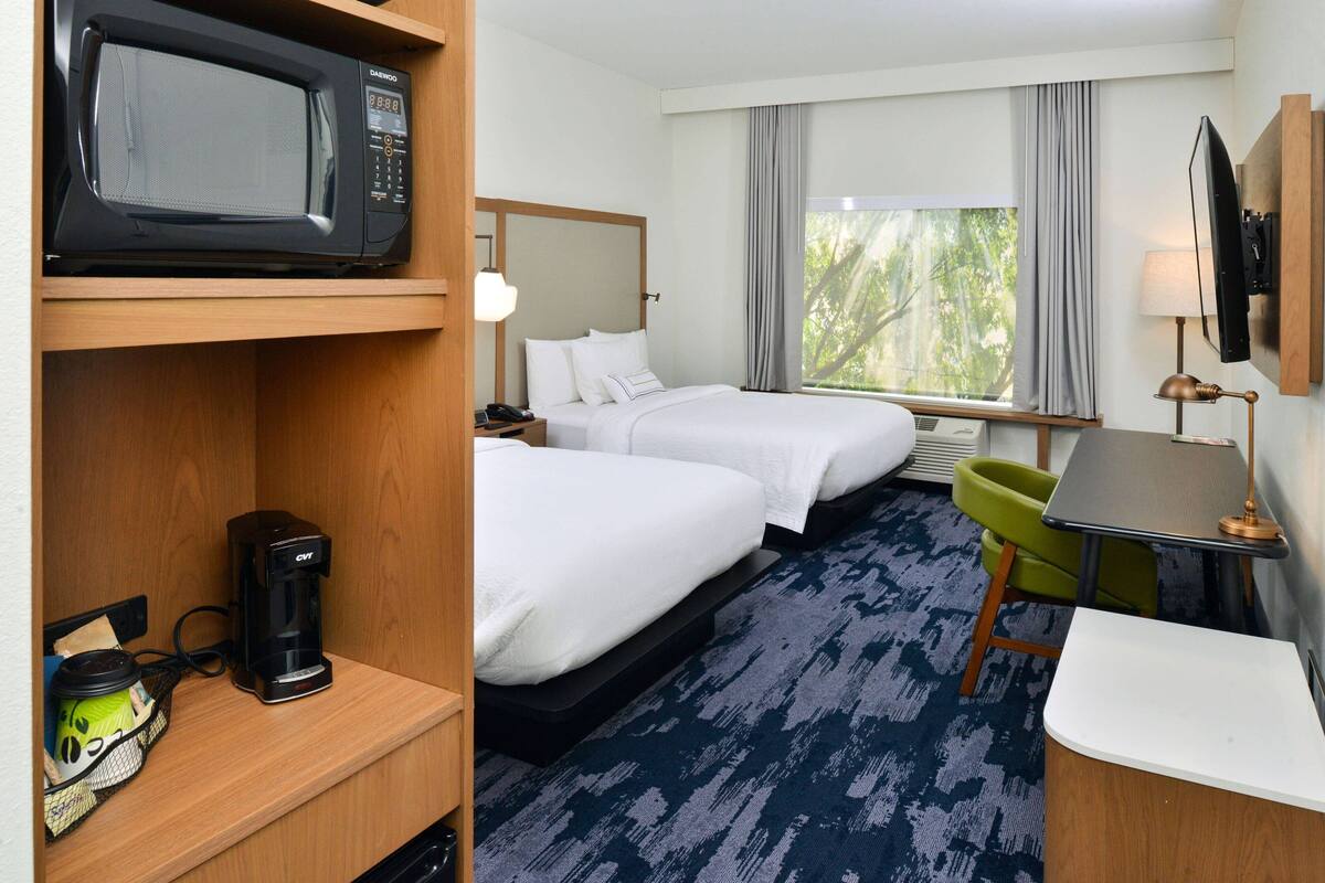 A hotel room with a bed, a desk, a chair, a microwave, a coffee maker, and a TV.