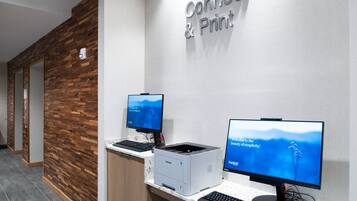 A reception area with a wooden wall, a sign that reads "Connect & Print," and two computer monitors on a desk with a printer.