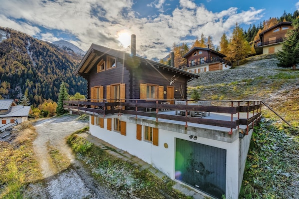 Un moderno chalet con fachada de madera, ventanas grandes y un balcón con vistas a un paisaje montañoso.