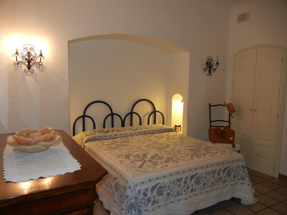 Un dormitorio con cama, mesita de noche, cómoda, lámpara de pared y puerta.