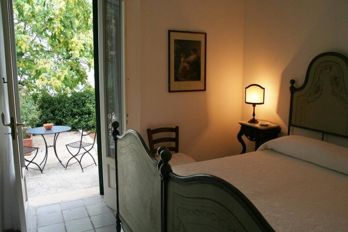 Une chambre à coucher avec un lit, une table de chevet avec une lampe, une chaise et un tableau encadré au mur.