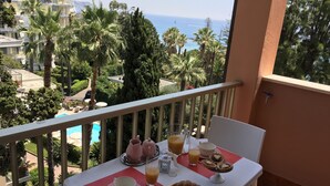 Ett balkongbord med frukostmat, med utsikt över en pool och havet.