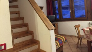 A staircase with wooden steps and a wooden handrail, a television on a wooden stand, a window with curtains, and a chair with a colorful cushion. - Room Apartment Luxury Duplex view Matterhorn skis - SAUNA - WIFI (Breuil-Cervinia)