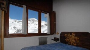 A room with a bed, a window with curtains, a radiator, and a view of snow-covered mountains. - Room Apartment Luxury Duplex view Matterhorn skis - SAUNA - WIFI (Breuil-Cervinia)