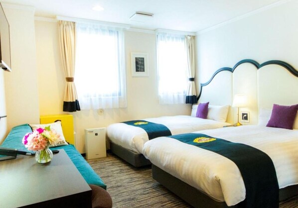 Habitación de hotel con dos camas, un escritorio y una pequeña mesa con un florero.