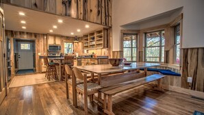 Una cocina amplia con muebles de madera, una mesa de comedor con bancos y grandes ventanales que dejan entrar luz natural.