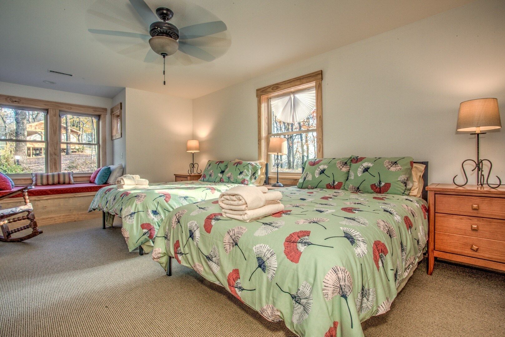 A bedroom with two beds, a ceiling fan, a window seat, and a wooden dresser.