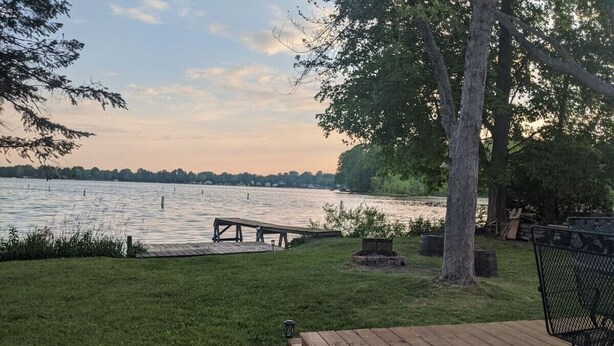 A wooden deck with a bench and a table, overlooking a lake with a dock and a fire pit. - Rustic Lakefront Cabin near Saugatuck&South Haven (Fennville)