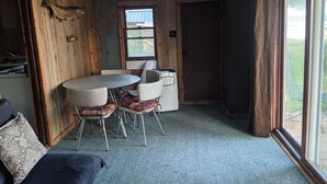 A room with a round table and four chairs, a small cabinet, and a window with curtains. - Rustic Lakefront Cabin near Saugatuck&South Haven (Fennville)