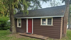A small, single-story building with a red door and two windows, surrounded by grass and trees. - Rustic Lakefront Cabin near Saugatuck&South Haven (Fennville)