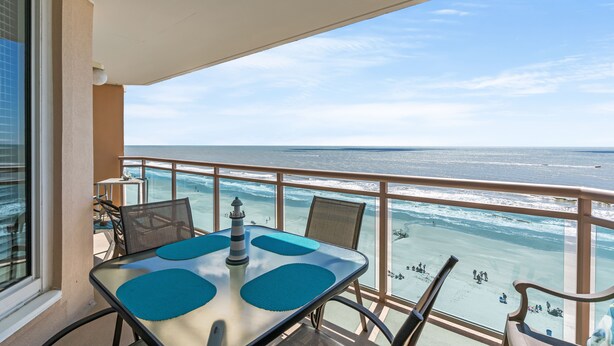 Een balkon met een tafel en stoelen, met uitzicht op een strand en zee.