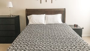 A bed with a patterned bedspread, a wooden headboard, two white pillows, a bedside table with a lamp, and a wall-mounted tree decoration. - Quiet home close to wec (Wilmington)