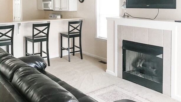 A modern kitchen with white cabinets, a microwave, and a flat-screen TV above the fireplace. There is a black leather sofa and two black chairs in the living area. - Quiet home close to wec (Wilmington)