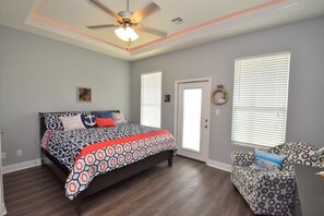 A bedroom with a bed, a ceiling fan, a door, and a window with blinds.