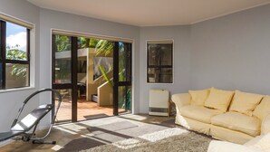 Ein Wohnzimmer mit gelbem Sofa, einem Sessel, einem großen Teppich und einer Glastür, die zu einem Außenbereich mit einer Treppe führt.