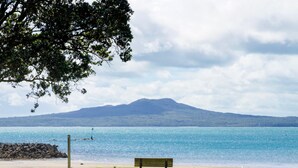 Eine Bank auf einer Wiese am Strand, im Hintergrund ein Berg.