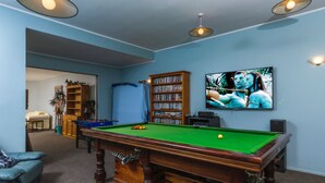 Ein Billardtisch mit Kugeln, ein Bücherregal und ein Fernseher in einem Zimmer mit blauen Wänden.