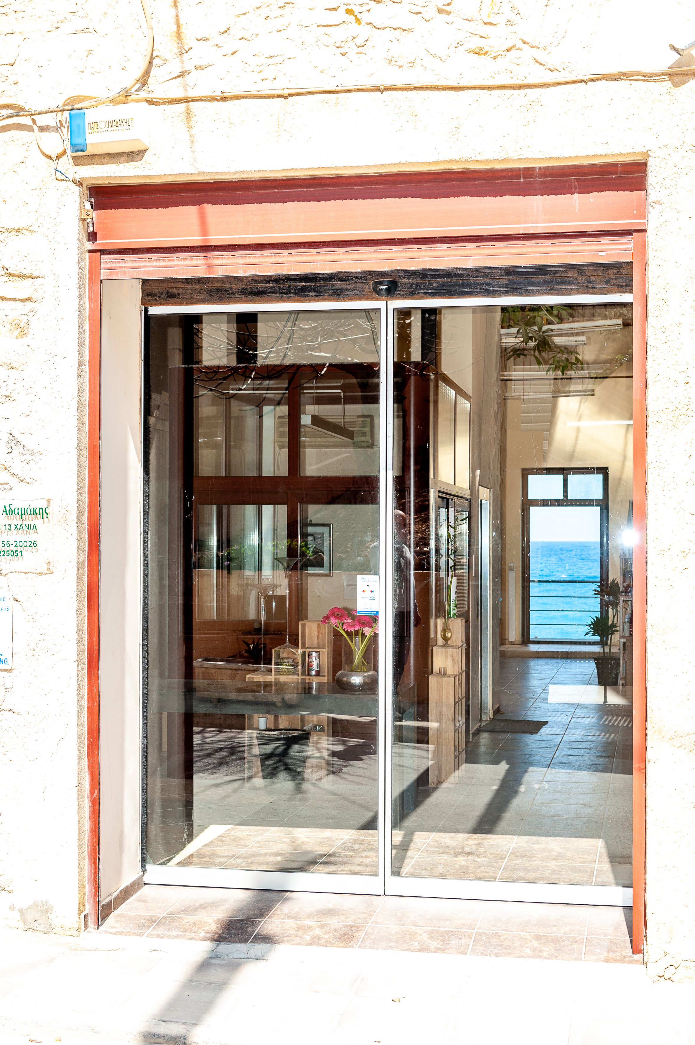 Entrada de hotel con puerta de cristal, vista al mar a través de la puerta y suelo de baldosas.
