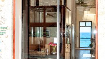 Entrada de hotel con puerta de cristal, vista al mar a través de la puerta y suelo de baldosas.