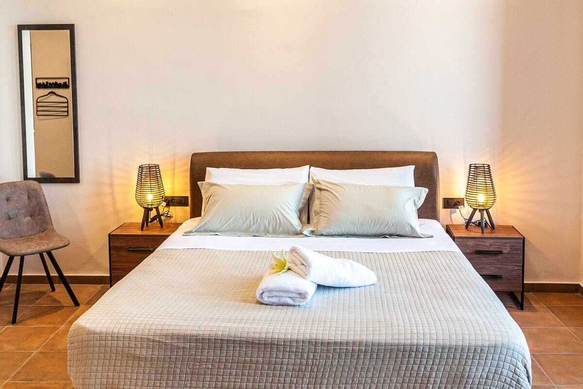A neatly made bed with a quilted bedspread, two bedside lamps, and a framed picture on the wall.