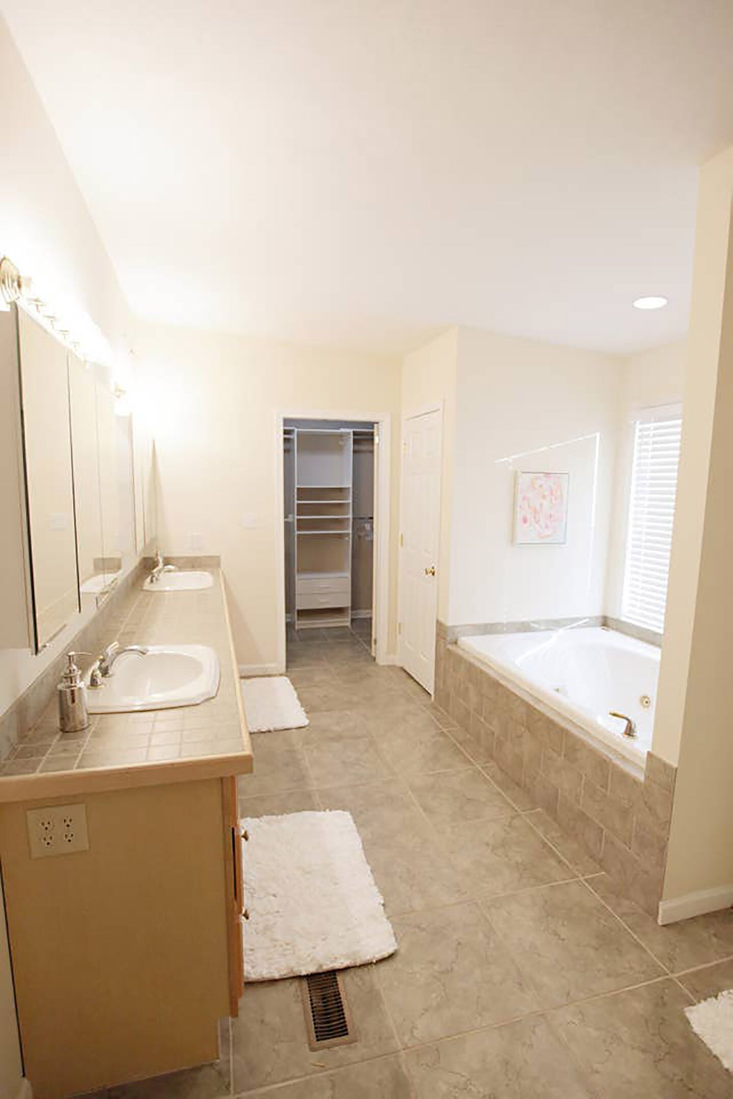 Un baño con dos lavamanos, una bañera, un vestidor y una puerta que da a otra habitación.