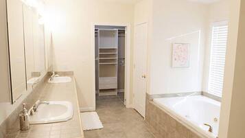 Un baño con dos lavamanos, una bañera, un vestidor y una puerta que da a otra habitación.