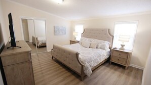 Une chambre à coucher comprenant un lit, des tables de chevet, une commode, un miroir et une fenêtre avec une lampe.