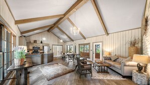 Un'ampia zona giorno con soffitto alto, travi in legno, un tavolo da pranzo e un angolo salotto accogliente con divano e lampada.