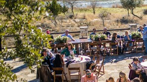 Un'area pranzo all'aperto con tavoli e sedie, un muro in pietra e un fiume sullo sfondo.