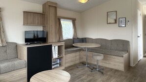 Un espacio habitable moderno y compacto con un televisor de pantalla plana, un sofá, una pequeña mesa redonda y una estantería.