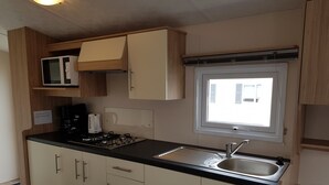 Una kitchenette compacta con microondas, estufa y lavamanos, armarios de madera y una ventana que proporciona luz natural.