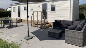 Una casa móvil con un patio amueblado, que incluye una mesa, sillas, un sofá y una sombrilla.