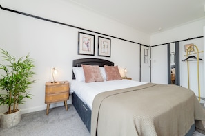 A bedroom with a bed, bedside tables, a lamp, a potted plant, and framed artwork on the wall.