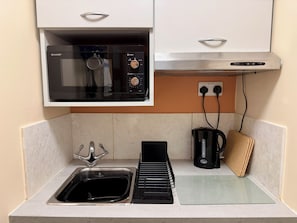 A compact kitchen with a built-in microwave, a kettle, a coffee maker, and a sink.