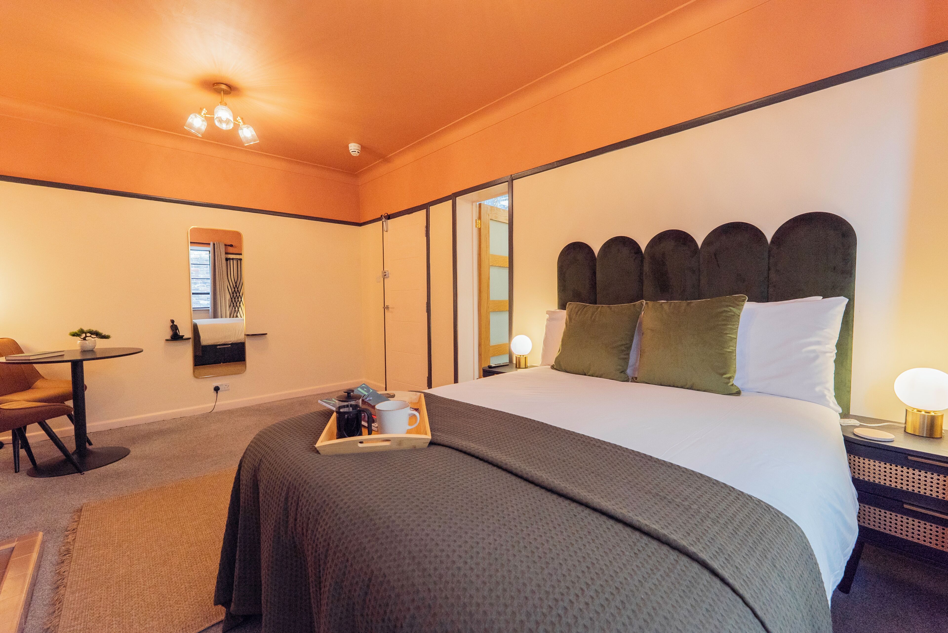 A hotel room with a bed, bedside table, nightstand, and a small table with a chair.