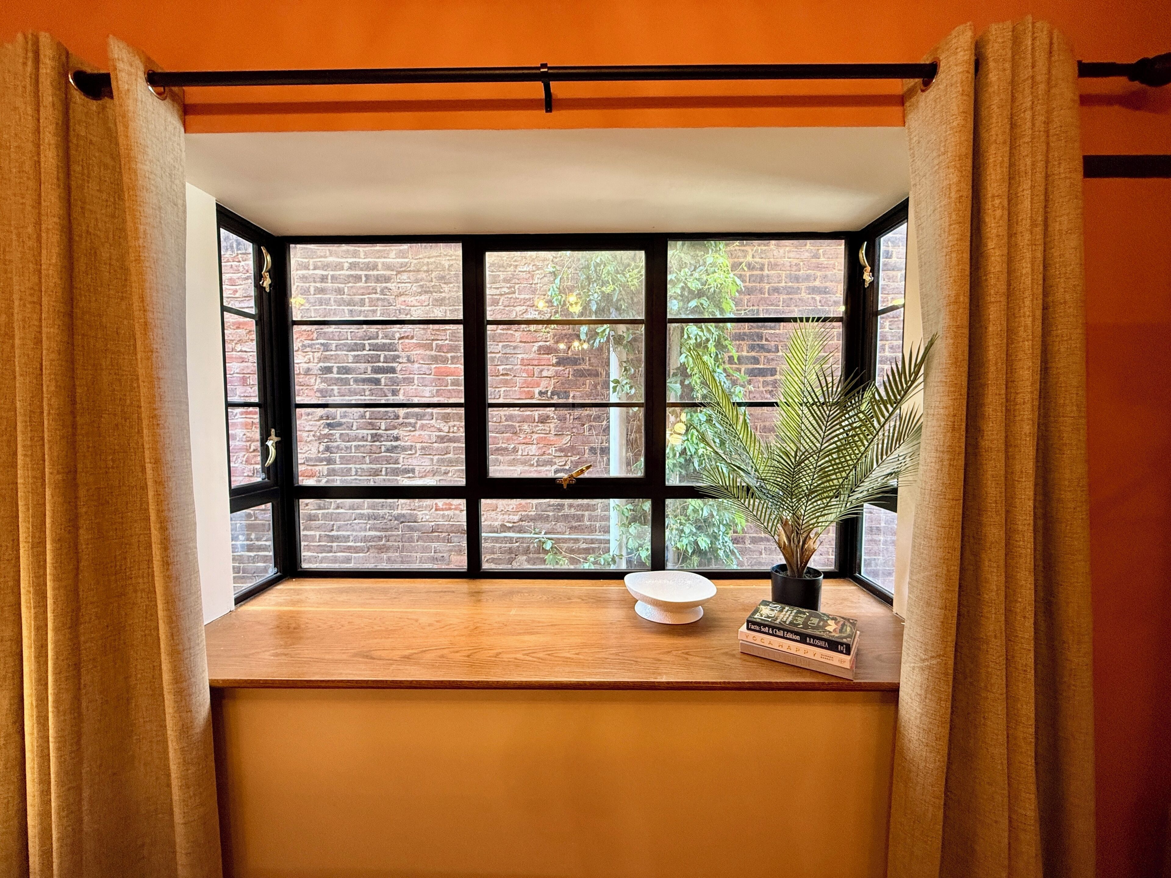 A room with a large window, a wooden table, a potted plant, and a book.