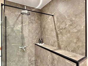 A modern shower with a glass enclosure, a handheld showerhead, and a shelf with toiletries.